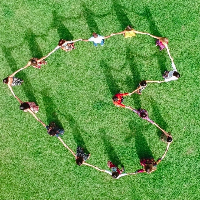 Vista aérea de um grupo de pessoas de mãos dadas formando um coração no gramado, projeto Bio Para Todos